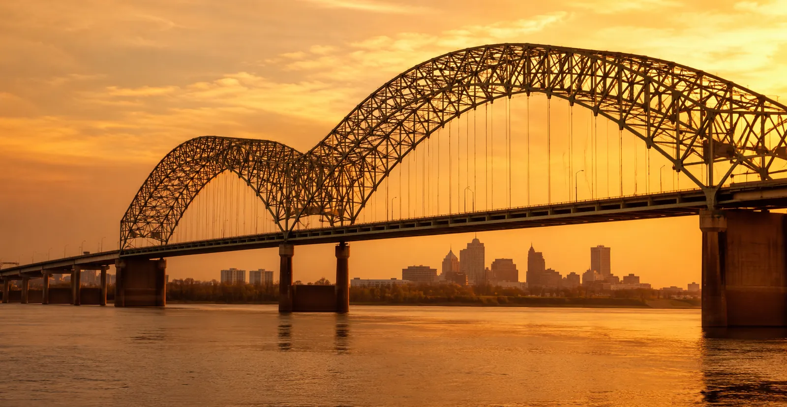 The Hernando de Soto Bridge over the Mississippi River at golden hour, with the Memphis skyline beyond